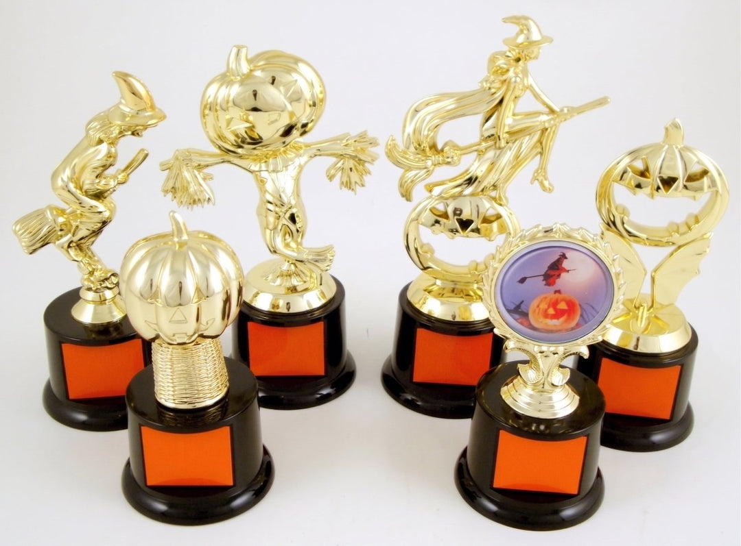Six gold-toned Halloween-themed trophy figures with black bases and orange square panels, arranged on a white studio background. Designs include a witch riding a broom, a scarecrow, a flying witch, a jack-o&