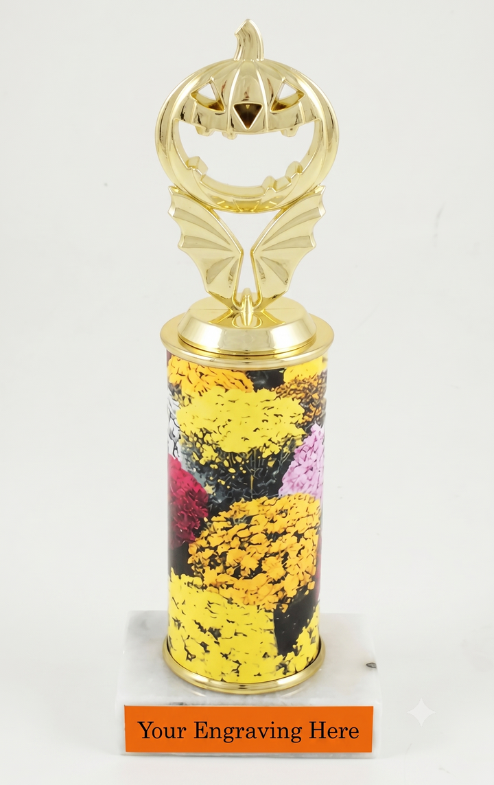 A Halloween-themed trophy featuring a gold-plated pumpkin topper with bat wings, a custom rolled column printed with yellow marigolds, and a white marble base with an orange plate  reading &