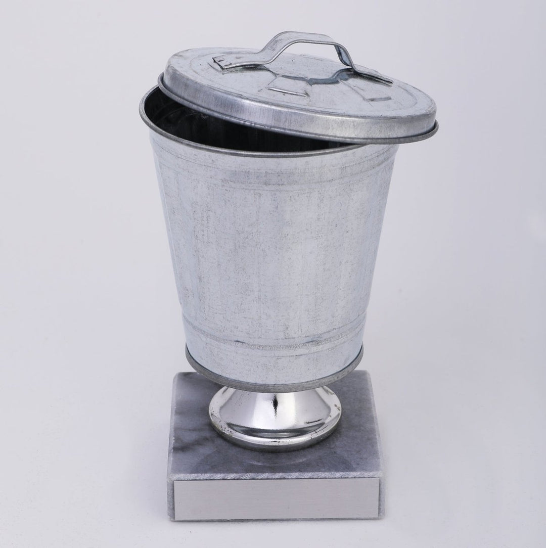 Galvanized metal wastebasket Trophy on a polished silver pedestal base with a grey marble base, photographed against a neutral light gray background