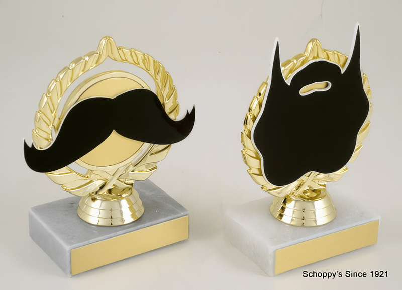 Two decorative trophy-style plaques on white marble bases with gold sides and tops. Each plaque features a black mustache or beard silhouette over a gold wreath design, shown against a plain light background.