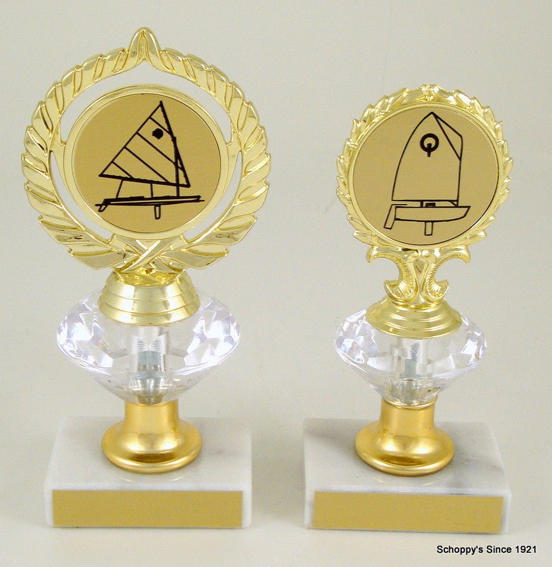 Two trophies with sailboat logos on diamond risers on white marble bases with gold engraving plates