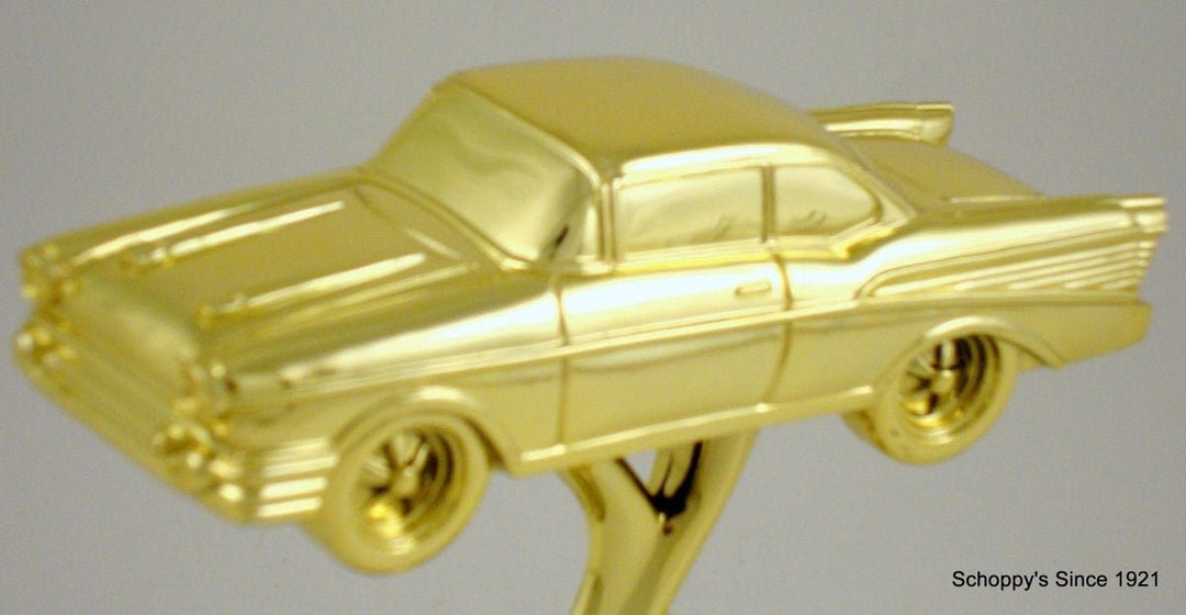 A shiny gold metallic model of a classic 1957 Chevrolet-style car mounted on a gold stand, photographed against a neutral gray background.